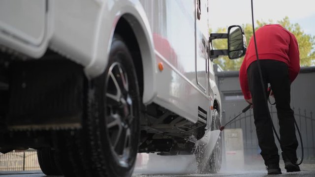 Seasonal RV Recreational Vehicle Motorhome Cleaning Using Pressure Washer. RV Camper Car Washing by Caucasian Men in His 30s.