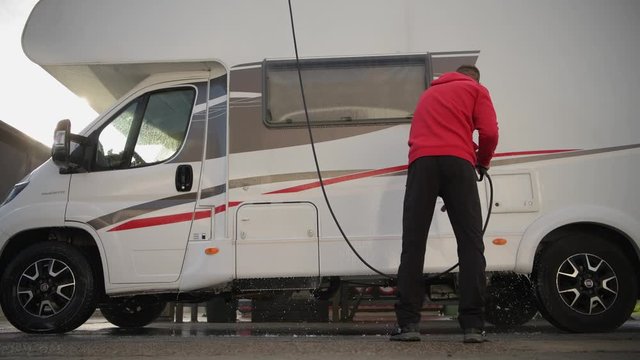 RV Camper Pressure Washing. Caucasian Motorhome Owner Cleaning His Vehicle After Season.
