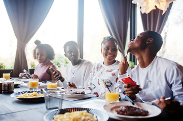 Happy african friends sitting, chatting in cafe and eat food. Group of black peoples meeting in restaurant and have dinner.
