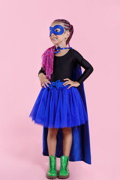Little girl plays superhero. Kid on the background of bright pink wall, wear in colorful clothes green boots, pink hair.