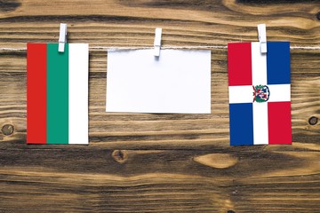 Hanging flags of Bulgaria and Dominican Republic attached to rope with clothes pins with copy space on white note paper on wooden background.Diplomatic relations between countries.