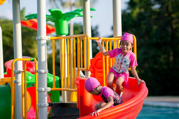 Happy kids playing on slider playground in swimming pool