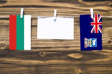 Hanging flags of Bulgaria and Falkland Islands attached to rope with clothes pins with copy space on white note paper on wooden background.Diplomatic relations between countries.