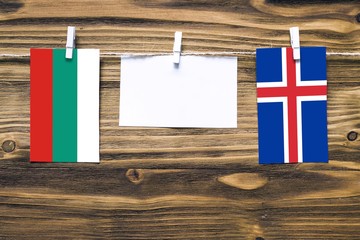 Hanging flags of Bulgaria and Iceland attached to rope with clothes pins with copy space on white note paper on wooden background.Diplomatic relations between countries.