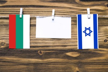 Hanging flags of Bulgaria and Israel attached to rope with clothes pins with copy space on white note paper on wooden background.Diplomatic relations between countries.