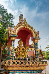 Obraz premium Ko Samui Island, Thailand - March 18, 2019: Wat Phra Yai Buddhist Temple on Ko Phan. Hindu 4-headed god Lord Brahma golden statue under eleborately decorated baldachin. Blue sky and green foliage.