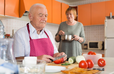 Senior man helping wife to cook