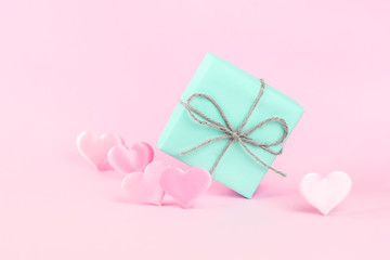 Gift box of blue color decorated with a string of twine on a pink background among pink silk hearts. Holiday concept. Place for text.
