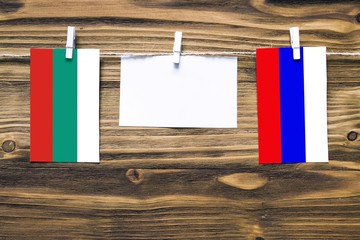 Hanging flags of Bulgaria and Russia attached to rope with clothes pins with copy space on white note paper on wooden background.Diplomatic relations between countries.