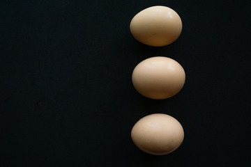 three uncooked eggs in raw from above point on black background
