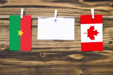 Hanging flags of Burkina Faso and Canada attached to rope with clothes pins with copy space on white note paper on wooden background.Diplomatic relations between countries.