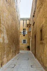 Typical Mdina street. Narrow medieval street of Mdina, also known as "Silent city", paved with stone slabs and surrounded with yellow limestone walls with white window shutters.