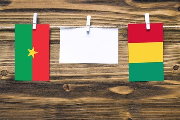 Hanging flags of Burkina Faso and Guinea attached to rope with clothes pins with copy space on white note paper on wooden background.Diplomatic relations between countries.