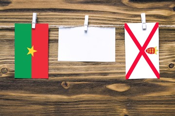 Hanging flags of Burkina Faso and Jersey attached to rope with clothes pins with copy space on...