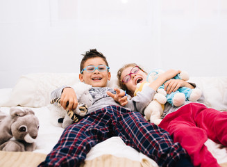 Children lying on a bed laughing surrounded by dolls.