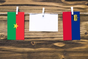 Hanging flags of Burkina Faso and Liechtenstein attached to rope with clothes pins with copy space on white note paper on wooden background.Diplomatic relations between countries.