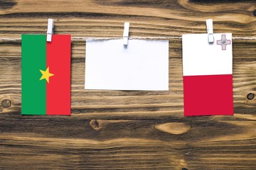 Hanging flags of Burkina Faso and Malta attached to rope with clothes pins with copy space on white note paper on wooden background.Diplomatic relations between countries.