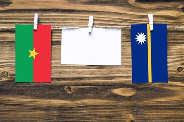 Hanging flags of Burkina Faso and Nauru attached to rope with clothes pins with copy space on white note paper on wooden background.Diplomatic relations between countries.