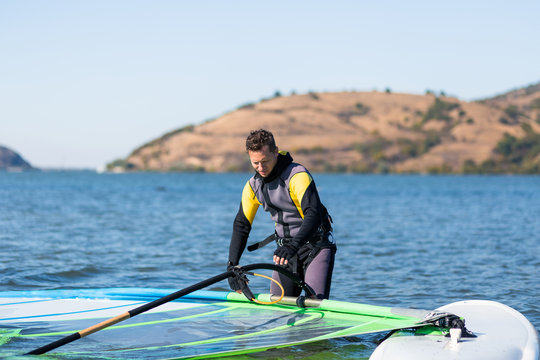 Sportsman preparing his windsurfing equipment in shallow water.