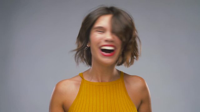 emotions and people concept - happy laughing young woman in mustard yellow top shaking head over grey background