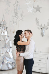 Beautiful couple in love hugging and kissing in Christmas interior. Young brunette woman in skirt and blouse hugging with handsome businessman in a white shirt. Loving married couple. New year