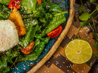Tasty salad with egg, tomato, guacamole sauce, with crackers, lime and herbs on a craft plate