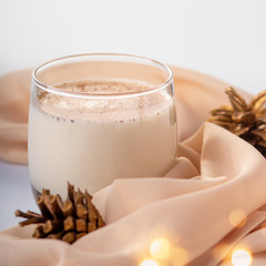 Traditional Christmas cocktail Eggnog with eggs, alcohol, grated nutmeg and cinnamon closeup, copy space, vertical frame. Sweet traditional drink on grey table with beige decorations and pine cones