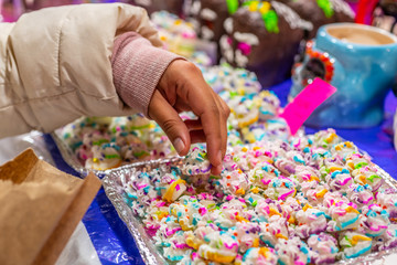 Hand of a woman taking one of the Calaveritas of sugar glass and sequin, typical sweets during the time of the day of the dead in Mexico, toy offerings made with crumbs and icing sugar