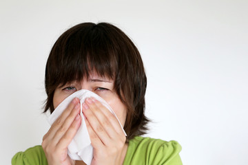 Runny nose and fever, woman blowing her nose in a handkerchief on white background. Unhappy girl suffering from rhinitis, concept of sick, colds and flu