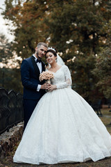 Naklejka premium Married couple embracing in the autumn park. Amazing smiling wedding couple with a bouquet of flowers. Pretty bride and stylish groom. Romantic married young family. Couple in love. Wedding.