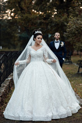 Amazing couple, happy bride and groom after wedding ceremony. Newlyweds are walking in the park. Wedding couple in autumn. Pretty bride and stylish groom. The bride plays with a veil