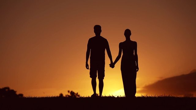 Young couple walking together at sunset holding hands. 