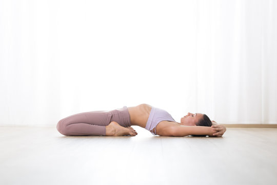 Portrait of gorgeous active sporty young woman practicing yoga in studio. Beautiful girl practice Supta Vajrasana, fixed firm yoga pose. Healthy active lifestyle, working out indoors in gym.