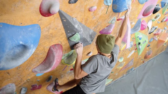 High angle view of young Caucasian man performing risky tricks on climbing wall in gym