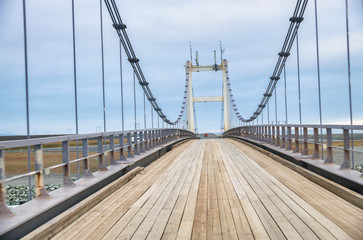 Fototapeta na wymiar Bridge with wooden pavement against cloudy sky