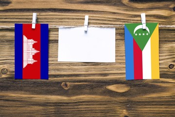 Hanging flags of Cambodia and Comoros attached to rope with clothes pins with copy space on white...