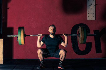 a young athlete performs squats with a barbell on his back in the gym for functional training, a...