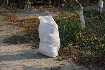 Big one white bag with garbage on the road in the grass