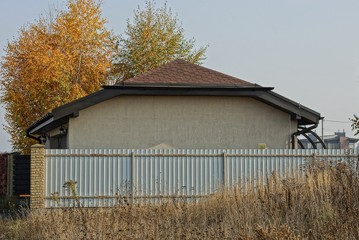 gray metal fence in dry grass and brown rural house