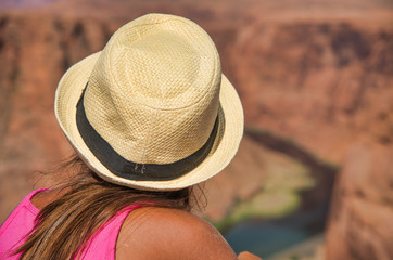 Young girl with straw hat mesmerized by Horseshoe Bend and Colorado River. Back view in summer season