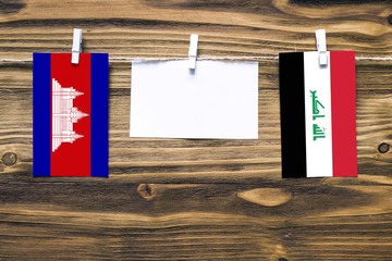 Hanging flags of Cambodia and Iraq attached to rope with clothes pins with copy space on white note paper on wooden background.Diplomatic relations between countries.