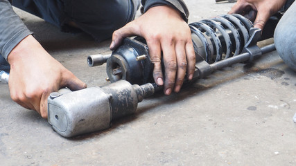 Asian mechanic using an air gun to unscrew of shock absorber replacement, Service industry of transportation