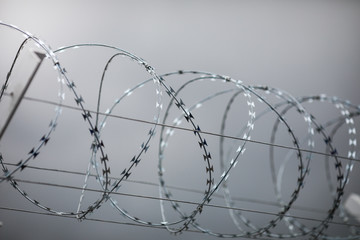 Shallow depth of field (selective focus) and filtered image with a razor wire on the outside wall of a governmental institution on a cloudy day.