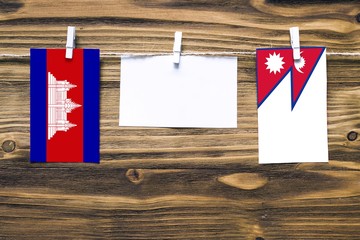 Hanging flags of Cambodia and Nepal attached to rope with clothes pins with copy space on white note paper on wooden background.Diplomatic relations between countries.