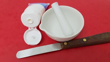 Ointment tube, mortar and spatula of pharmacy laboratory on red cardboard