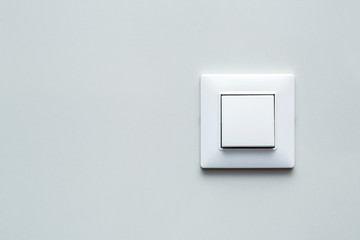 a light switch, a plastic mechanical button of white color installed on a light wall with copy space for text.