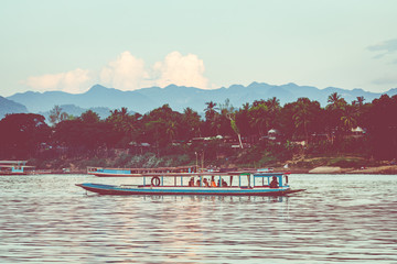 Traditional Long Boat on the Mekong River and mountains view in Luang Prabang, Laos.