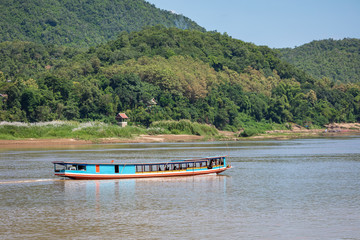 Traditional Long Boat on the Mekong River and mountains view in Luang Prabang, Laos.