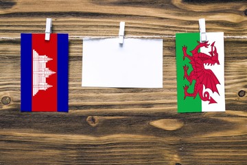 Hanging flags of Cambodia and Wales attached to rope with clothes pins with copy space on white...