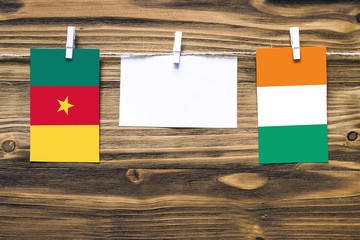 Hanging flags of Cameroon and Cote D'Ivoire attached to rope with clothes pins with copy space on white note paper on wooden background.Diplomatic relations between countries.